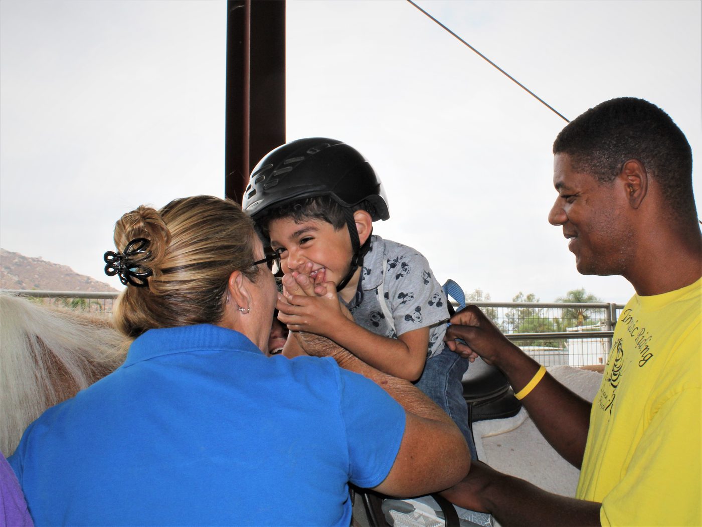 A child laughing with his instructors on horseback during a therapy session