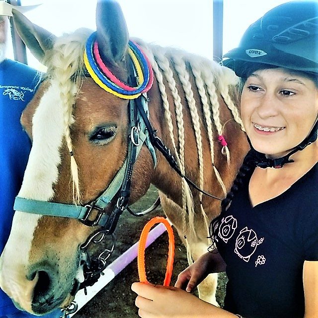 A teen volunteer smiling beside a horse with colorfully braided mane