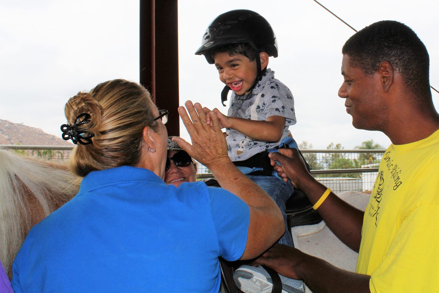 A young rider high-fiving his instructor while seated on a therapy horse